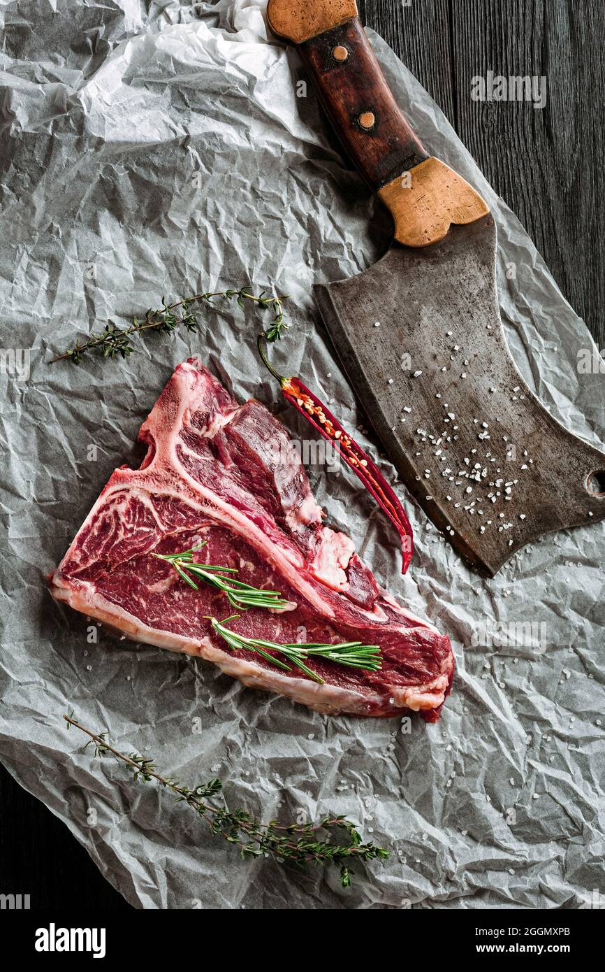 Bistecche di t-bone crude stagionate e secche per grigliare con erbe fresche e sfaldatura Foto Stock