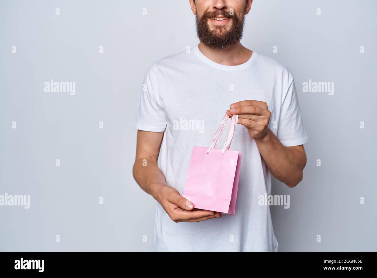 Uomo allegro in t-shirt bianca con rosa piccolo pacchetto regalo sfondo  chiaro Foto stock - Alamy