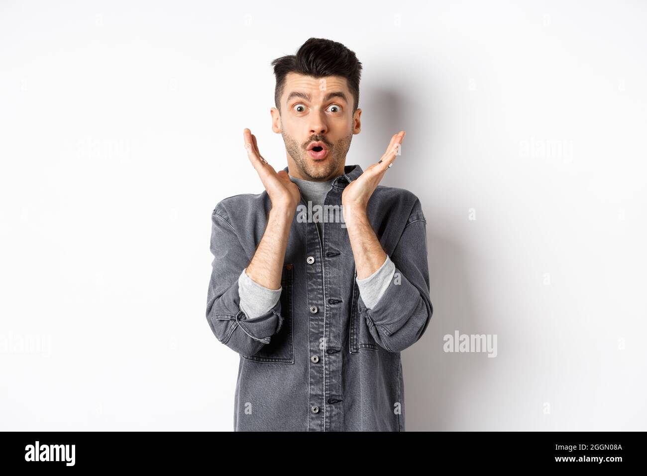L'uomo sorpreso che gasting eccitato, dica WOW e guardi la pubblicità stupefacente, in piedi su sfondo bianco Foto Stock