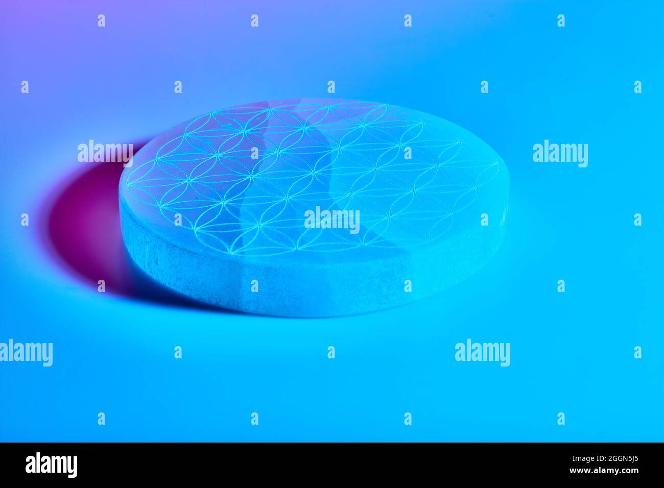 Pietra rotonda con intaglio sotto luci al neon blu viola e rosse Foto Stock