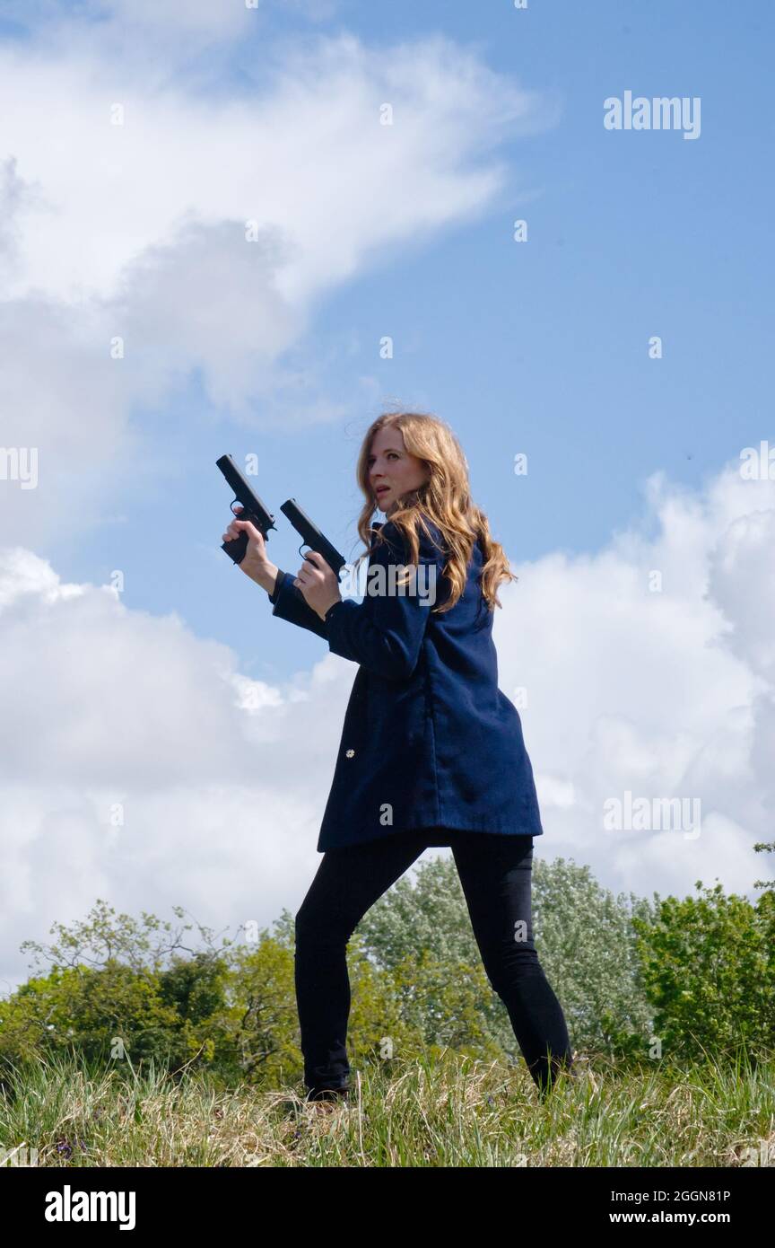 donna con pistola che indossa panni scuri su erba hillock con nuvole tempestose nel cielo (copertina libro) Foto Stock