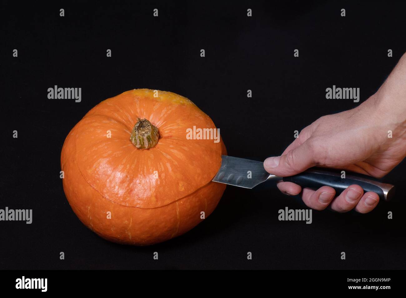 La mano tiene un coltello e taglia una zucca arancione rotonda, isolata su sfondo nero, primo piano, spazio di copia. Istruzioni dettagliate per la preparazione di un martinetto Foto Stock