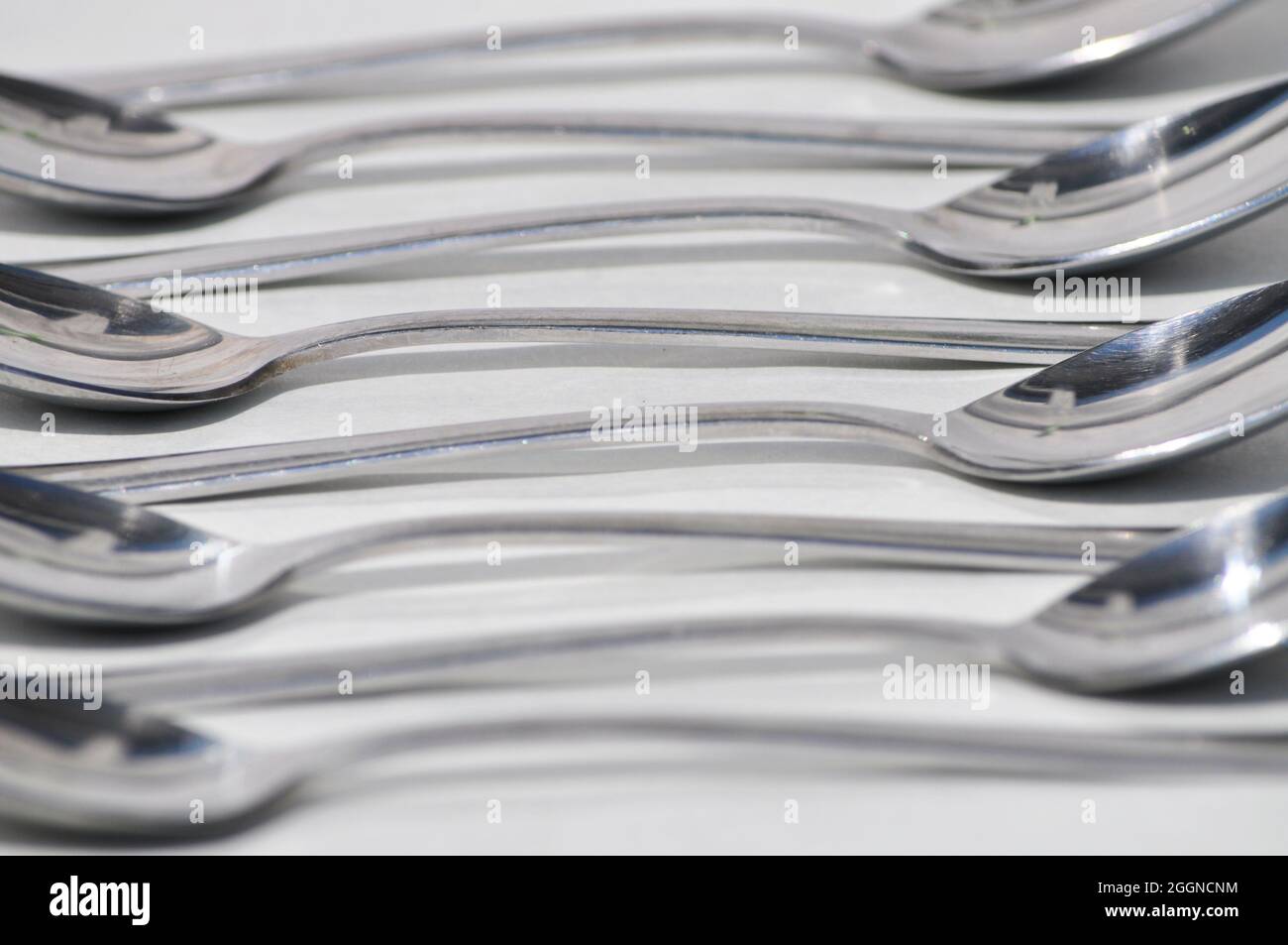 Cucchiai di acciaio inossidabile disposti su sfondo bianco in un motivo ricorrente Foto Stock