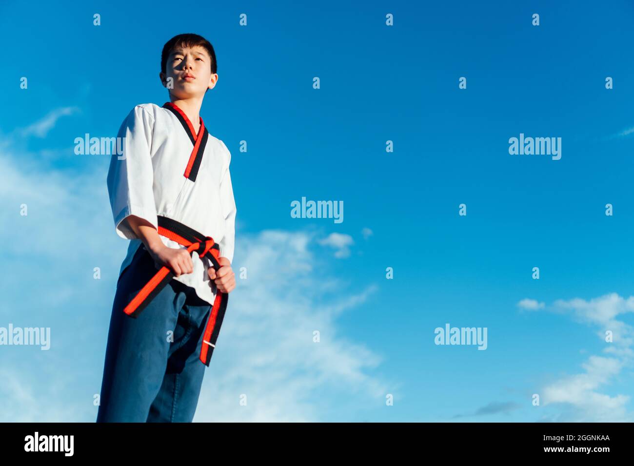 Ritratto di un giovane giapponese nel suo taekwondo kimono che tiene la cintura nera del suo kimono di arti marziali. Pantaloni kimono bianco e karate blu Foto Stock