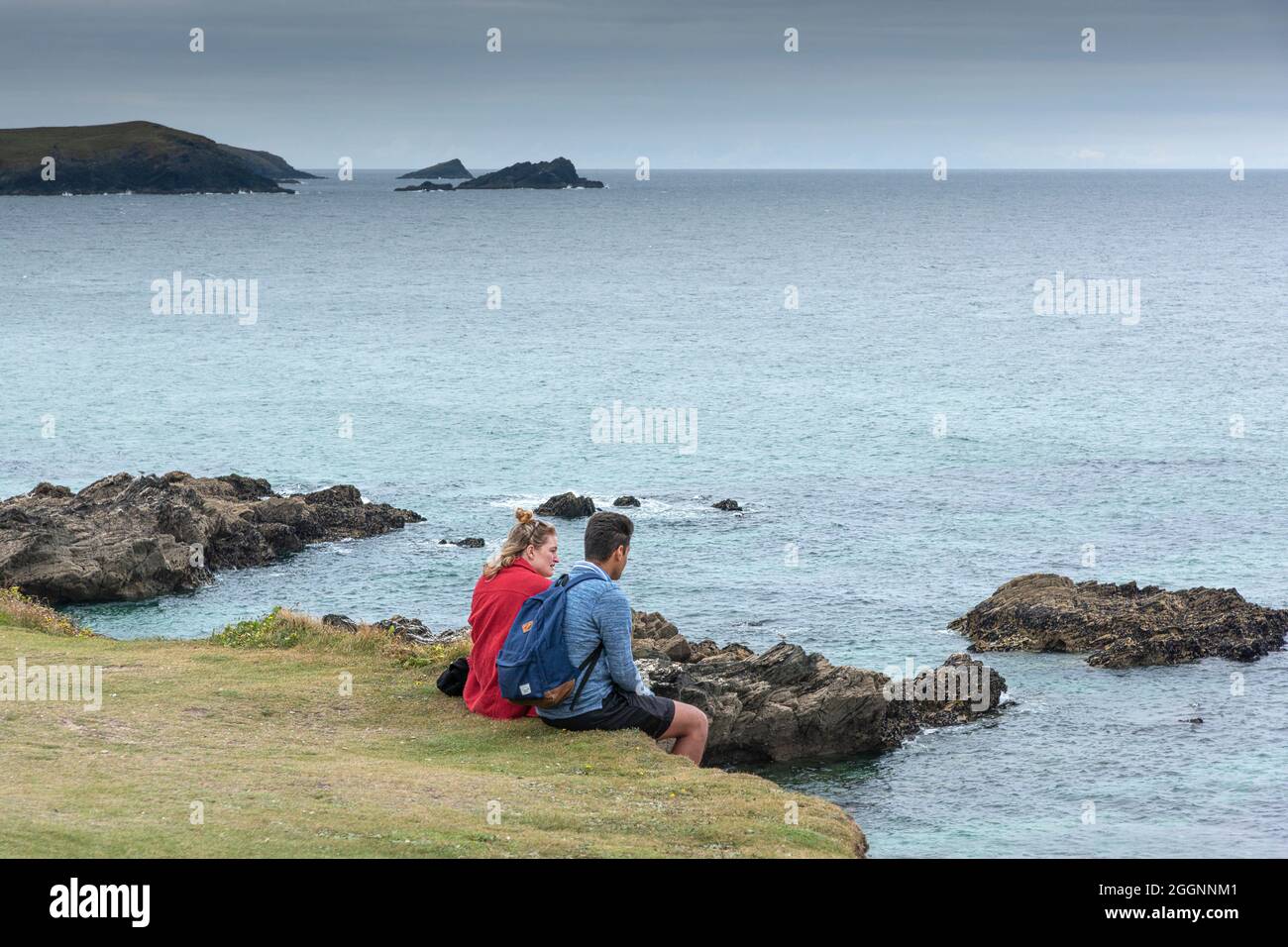 Una coppia in vacanza seduta insieme sulla costa a Newquay che si affaccia sul Mar Celtico. Foto Stock