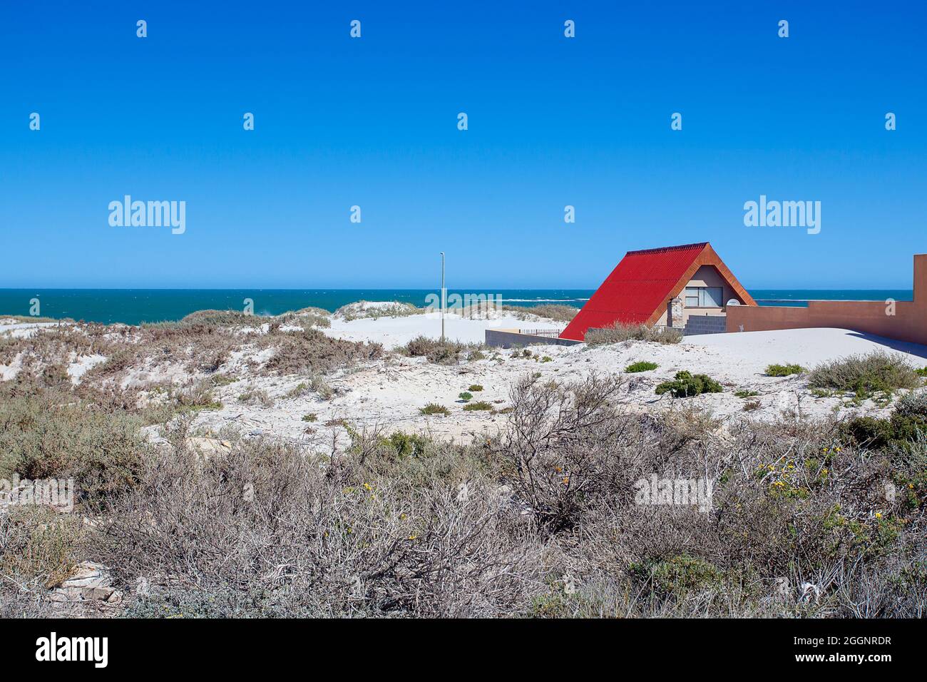 Contrasto costiero: Una casa dal tetto rosso tra sabbia e mare Foto Stock