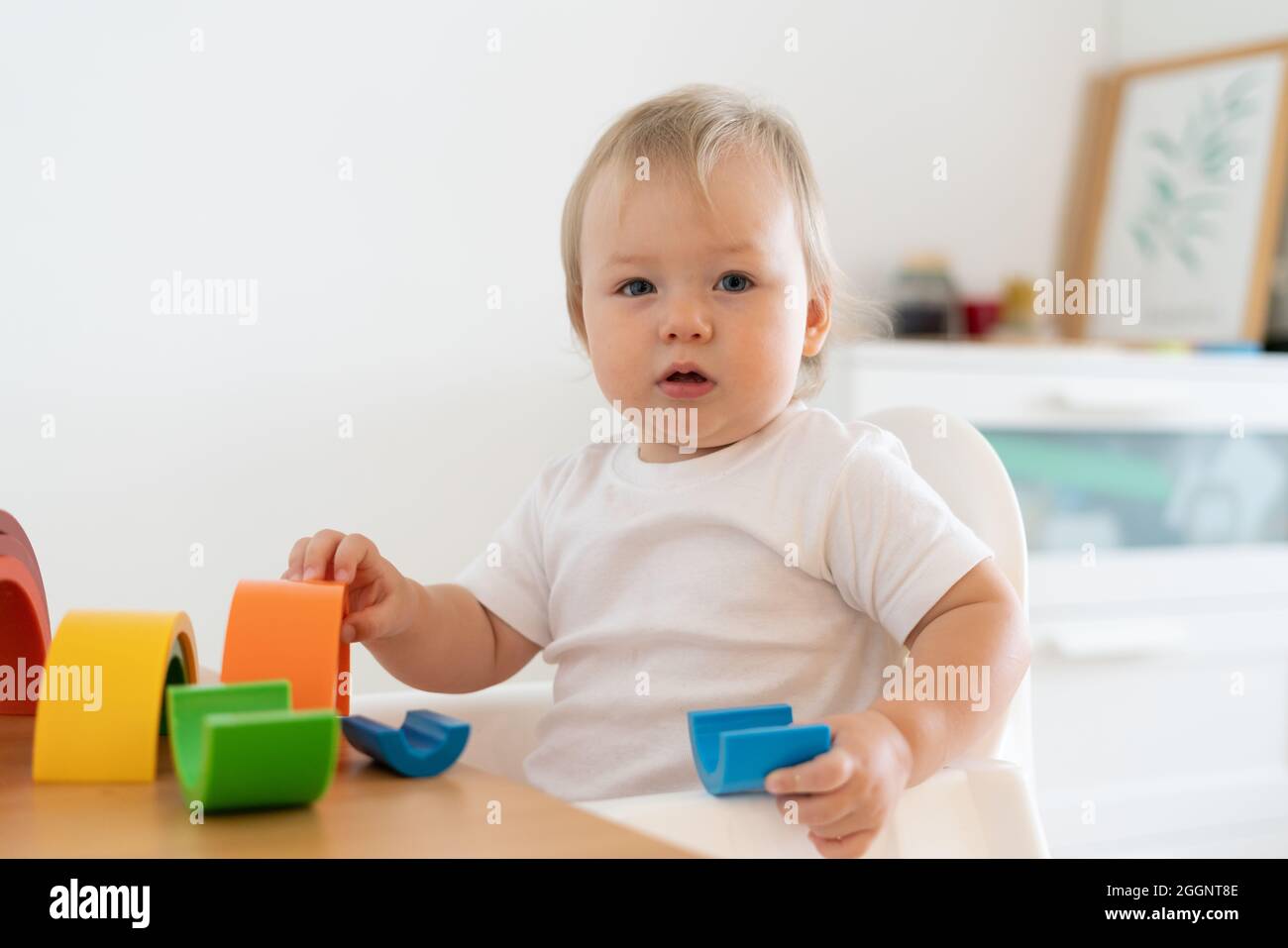 Biondo biondo con occhi blu che gioca con figure geometriche in plastica. Sviluppo del motore del bambino all'asilo Foto Stock