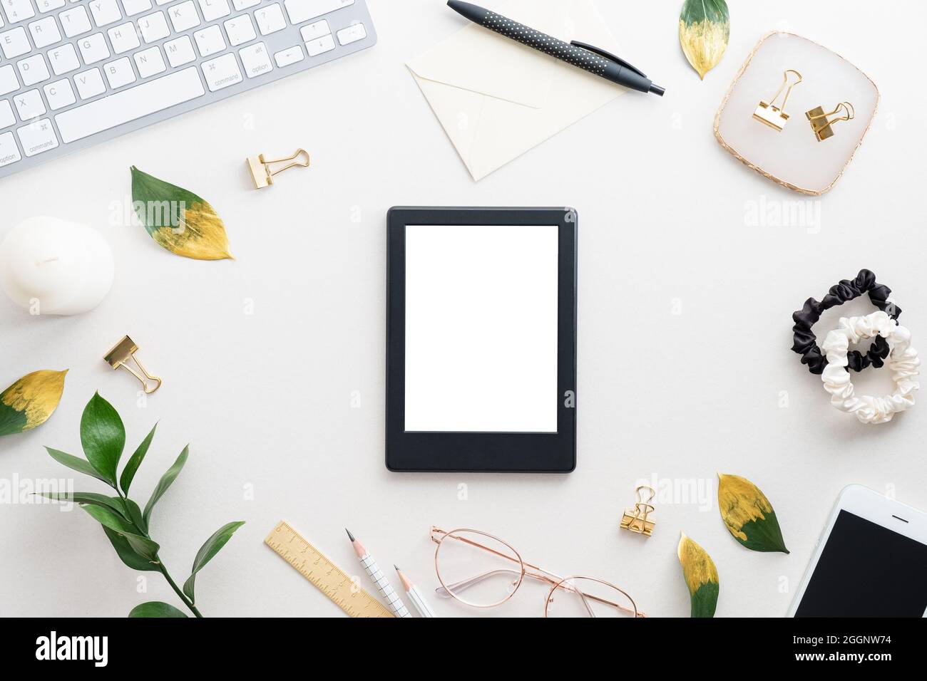 Tavolo da scrivania femminile con ebook da tablet con schermo vuoto, tastiera, foglie dorate su sfondo bianco. Spazio di lavoro elegante. Disposizione piatta, vista dall'alto. Foto Stock