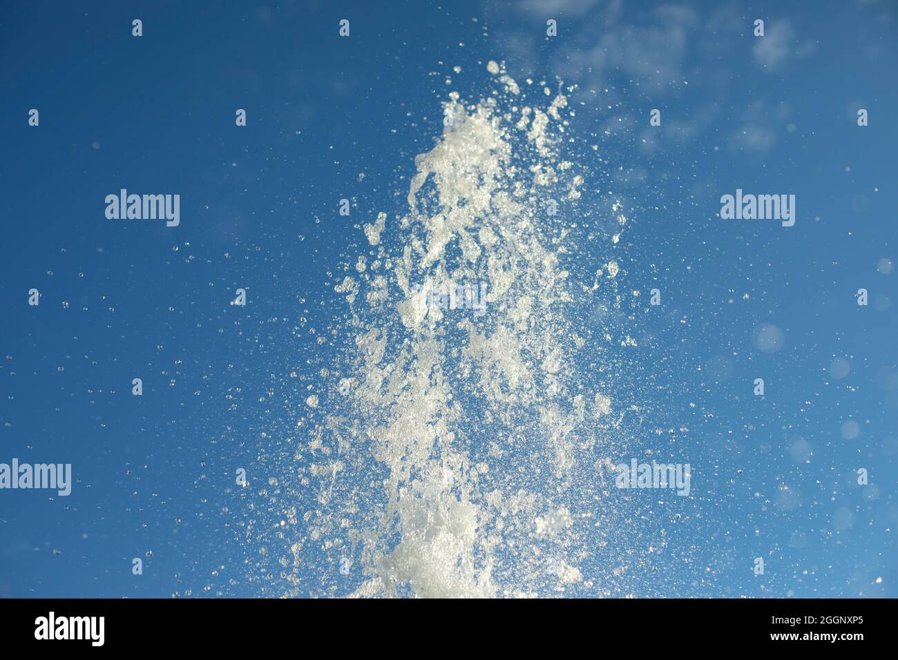 Spruzzi d'acqua nell'aria. Un jet di fantasia sullo sfondo del cielo. Piccole gocce volano ai lati. Foto Stock