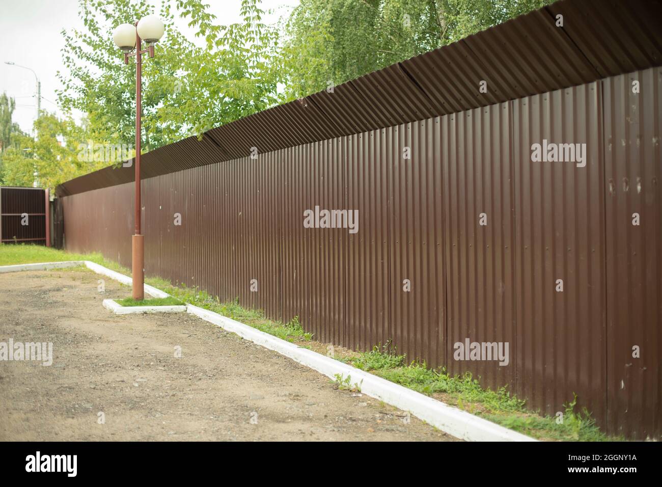 Una recinzione marrone racchiude l'area chiusa. Recinzione in metallo lungo il parcheggio. Protezione completa con recinzione solida. Foto Stock