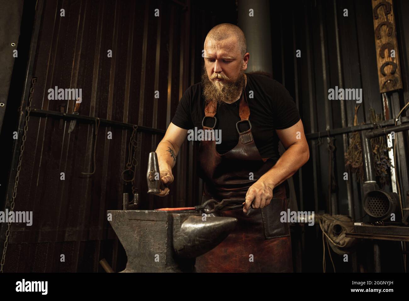 L'uomo bearded, fabbro forgiando manualmente il metallo fuso sull'incudine in fondente con i fuochi d'artificio della scintilla. Concetto di lavoro, professioni retrò, famiglia Foto Stock