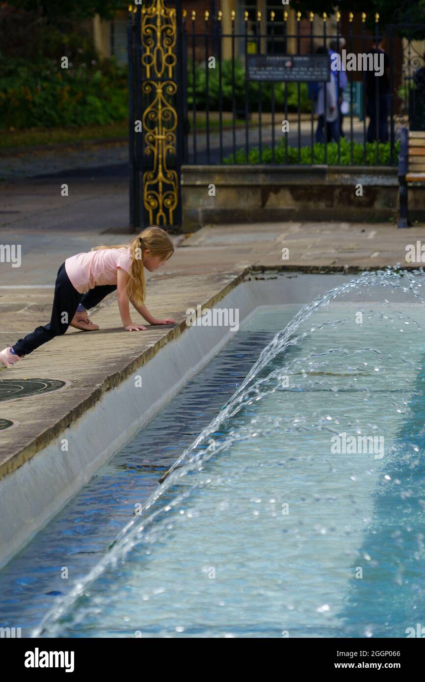 Una giovane ragazza che si inginocchia in una fontana situata accanto alla York Art Gallery a York, North Yorkshire, Inghilterra, Regno Unito. Foto Stock