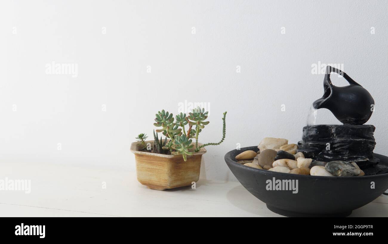 Zen fontana d'acqua e una piccola pianta succulenta posta sopra un tavolo bianco di legno. Una parete bianca brillante come sfondo Foto Stock