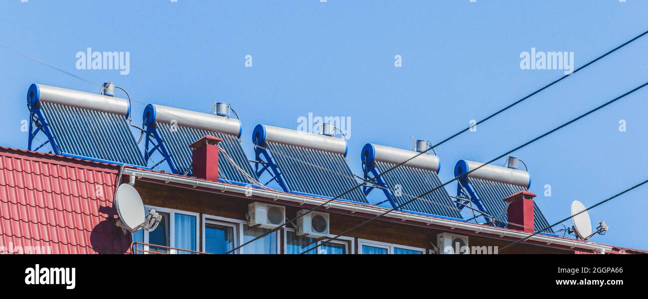 Pannelli solari termici e scaldabagno tecnologie alternative di riscaldamento dell'acqua sul tetto dell'hotel contro il cielo blu all'aperto. Foto Stock