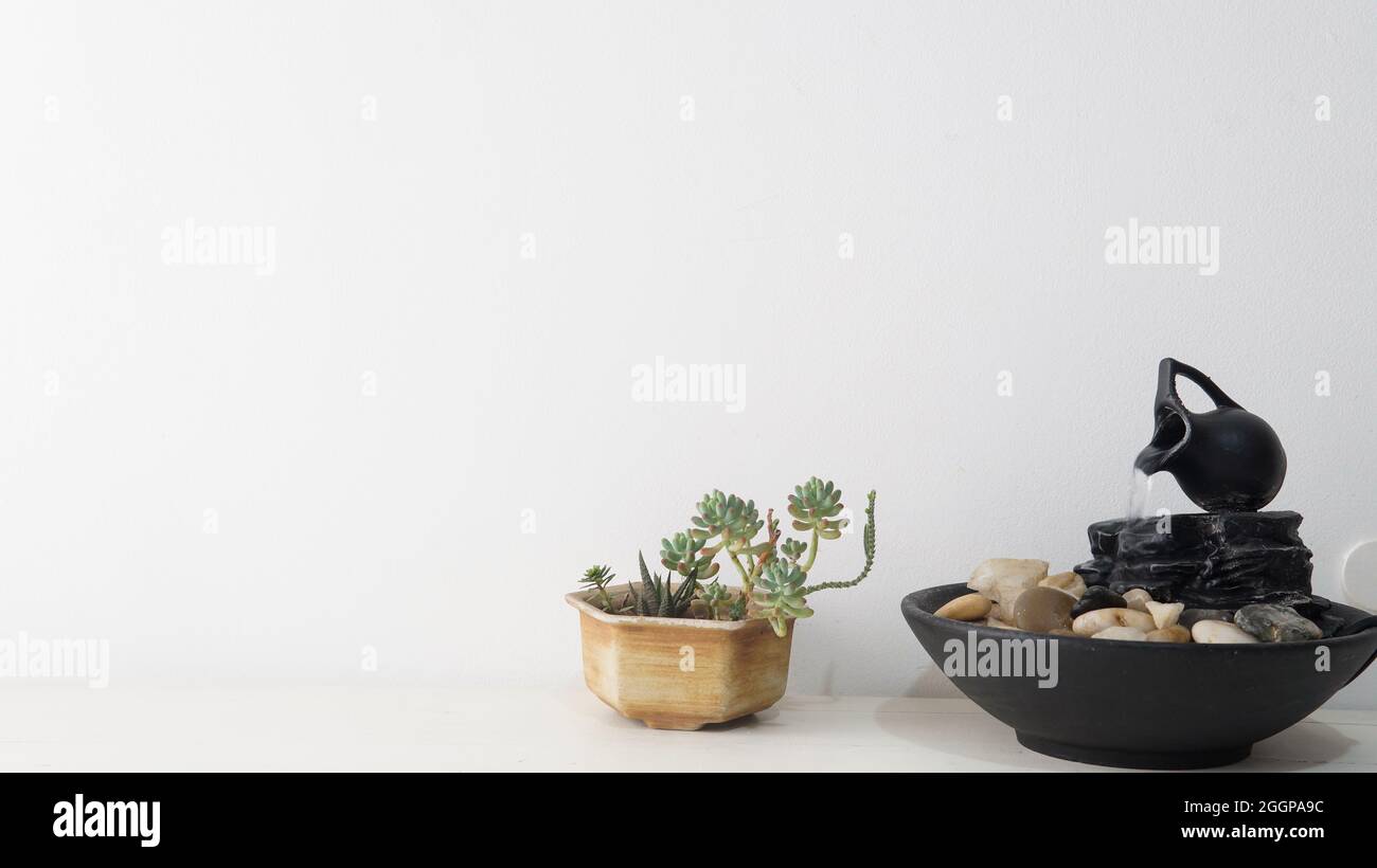 Zen fontana d'acqua e una piccola pianta succulenta posta sopra un tavolo bianco di legno. Una parete bianca brillante come sfondo Foto Stock