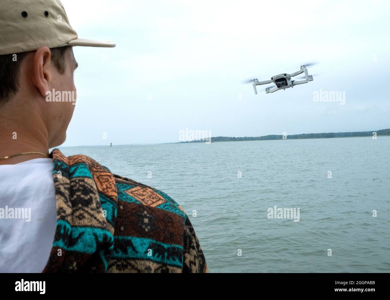 Giovane uomo che opera il drone di fotografia aerea su una piccola barca Foto Stock