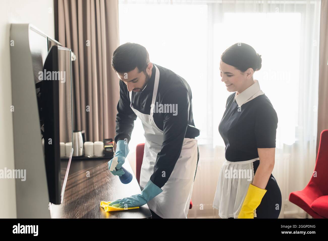 cameriera sorridente che guarda il collega che pulisce la superficie di legno con lo straccio Foto Stock