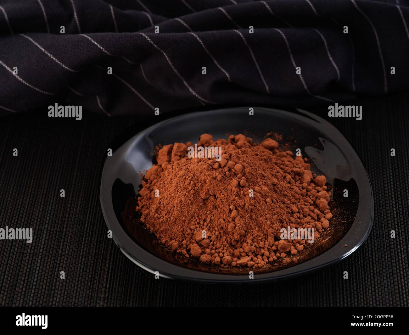 Polvere di cacao in un piatto nero. Tasto basso. Primo piano. Foto Stock