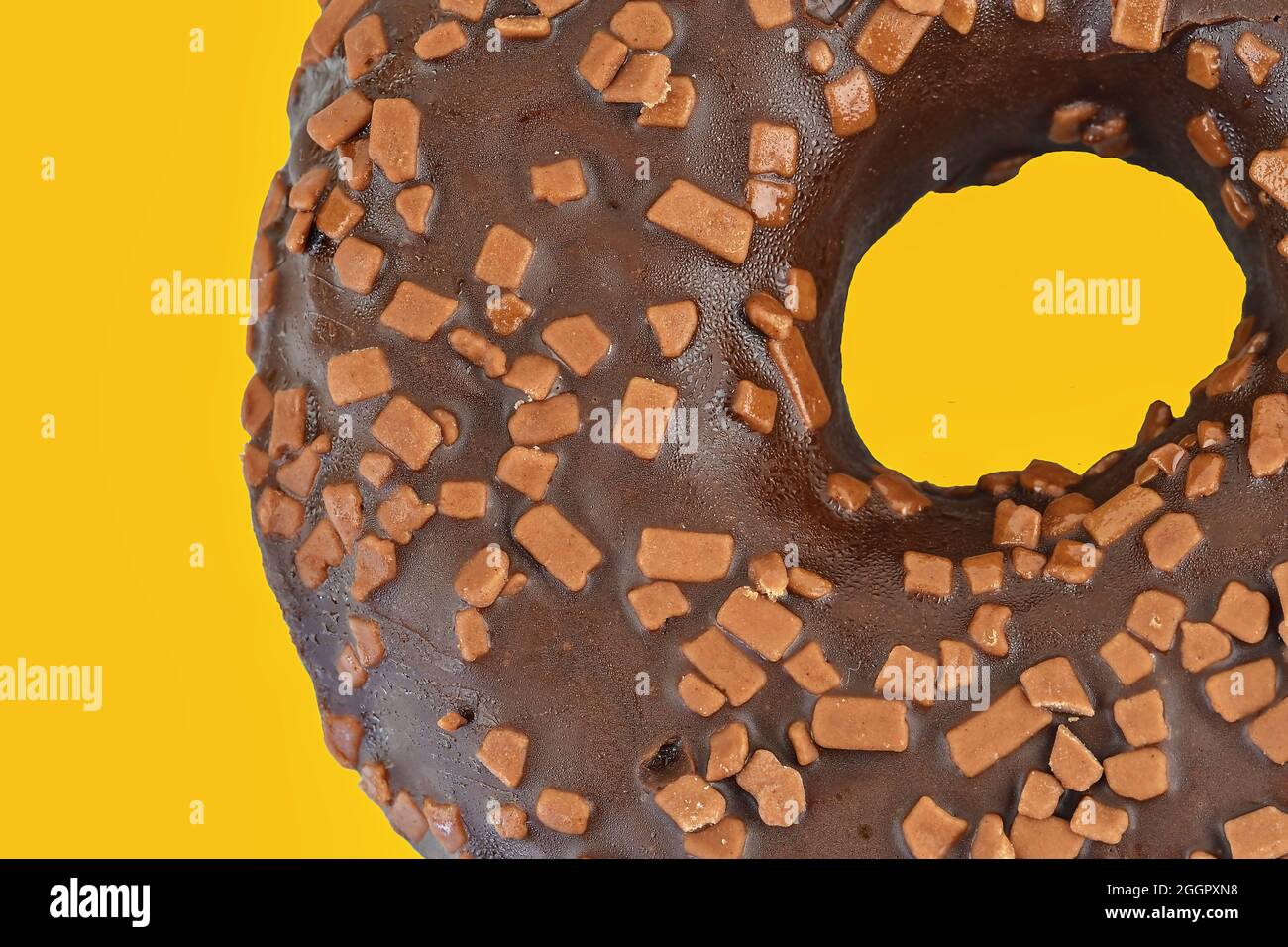Ciambella al cioccolato con spolverini su sfondo giallo. Zucchero, dolci, snack, cibo spazzatura concetto. Vista dall'alto. Spazio per il testo. Disposizione piatta Foto Stock