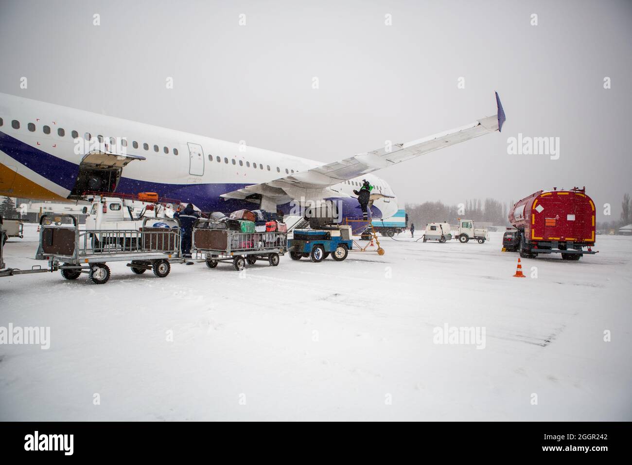 carico bagagli in aeroporto in inverno. Bagagli in cart vicino aereo in inverno. Aereo passeggeri in inverno all'aeroporto ha caricato il bagaglio prima della partenza Foto Stock