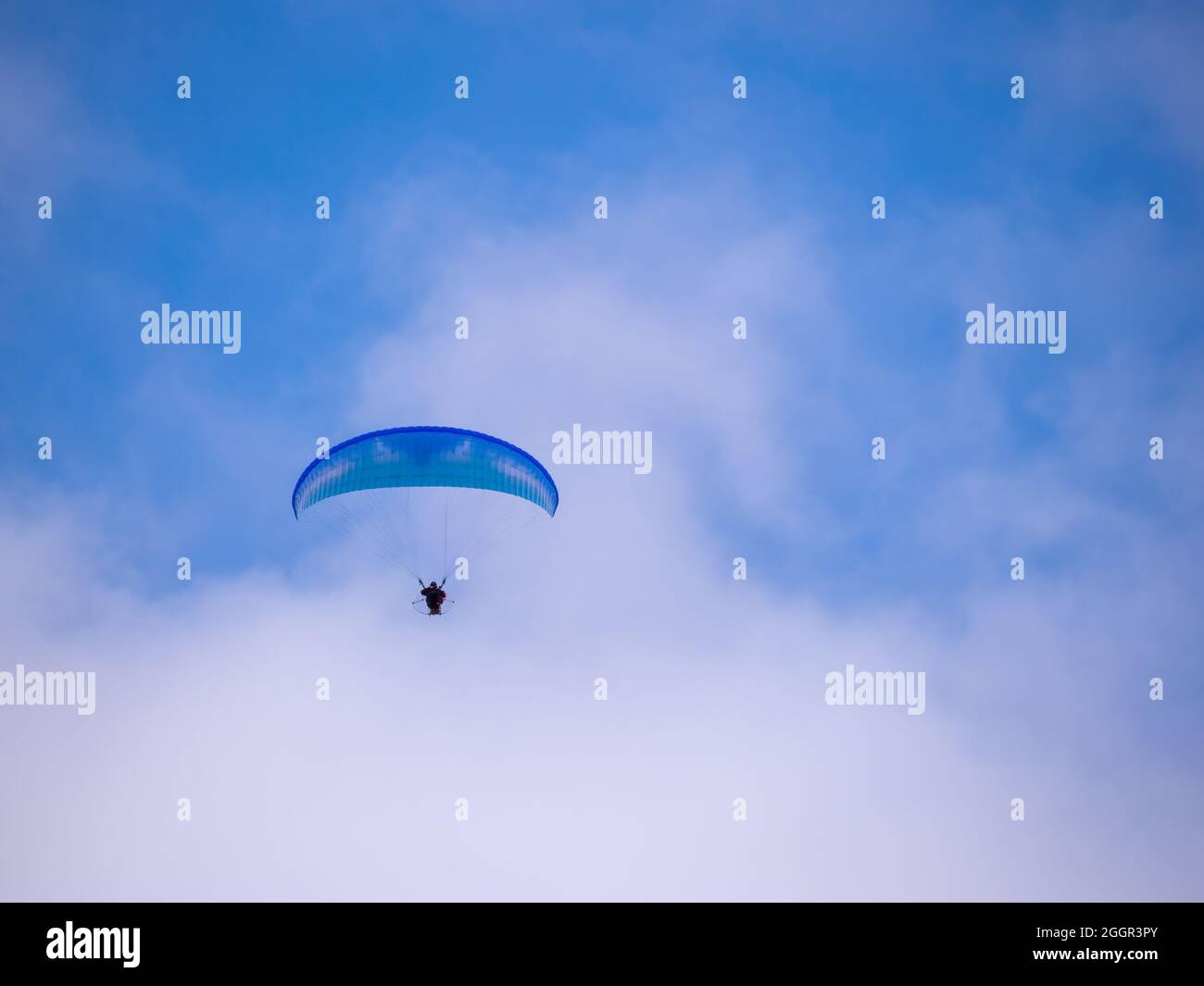 Parapendio blu inidentificabile contro il cielo blu con le nuvole. REGNO UNITO. Foto Stock
