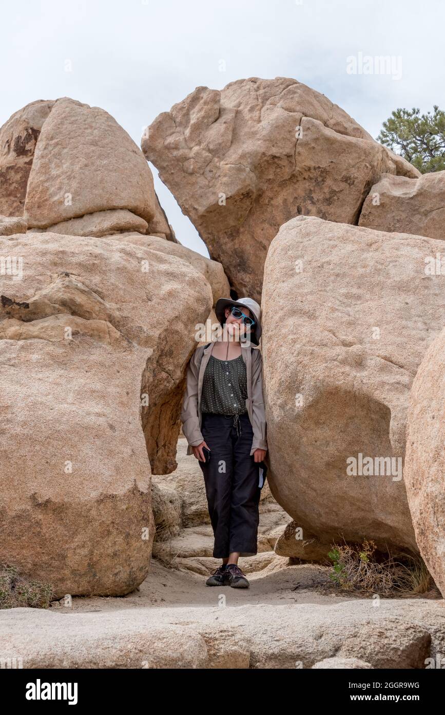 Una ragazza teen si ferma per una divertente foto in posa nello spazio stretto tra grandi massi nella valle nascosta al Joshua Tree National Park. Foto Stock