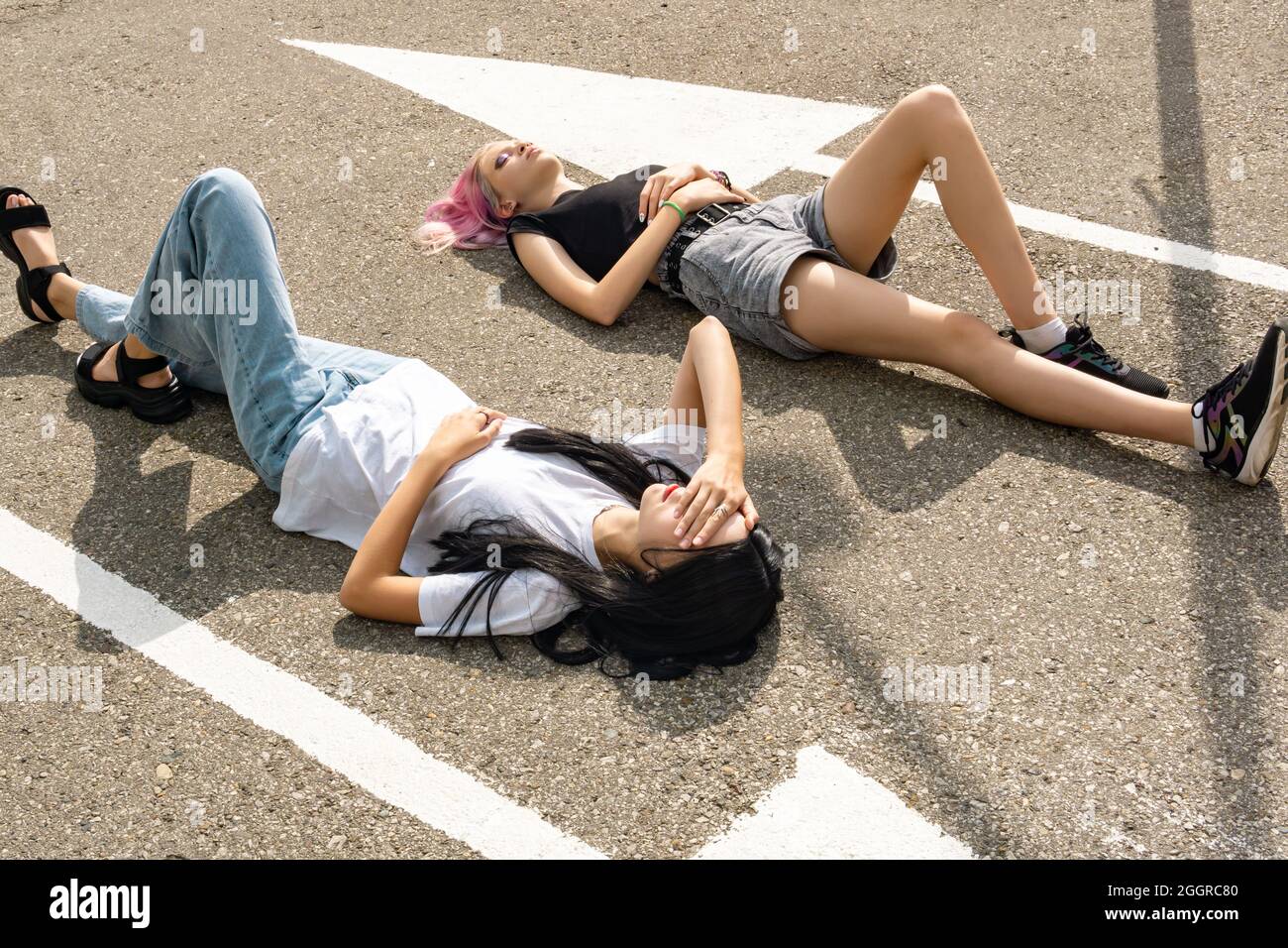 due ragazze teenager hanno divertimento che giacciono su una strada vuota parallela alle marcature Foto Stock