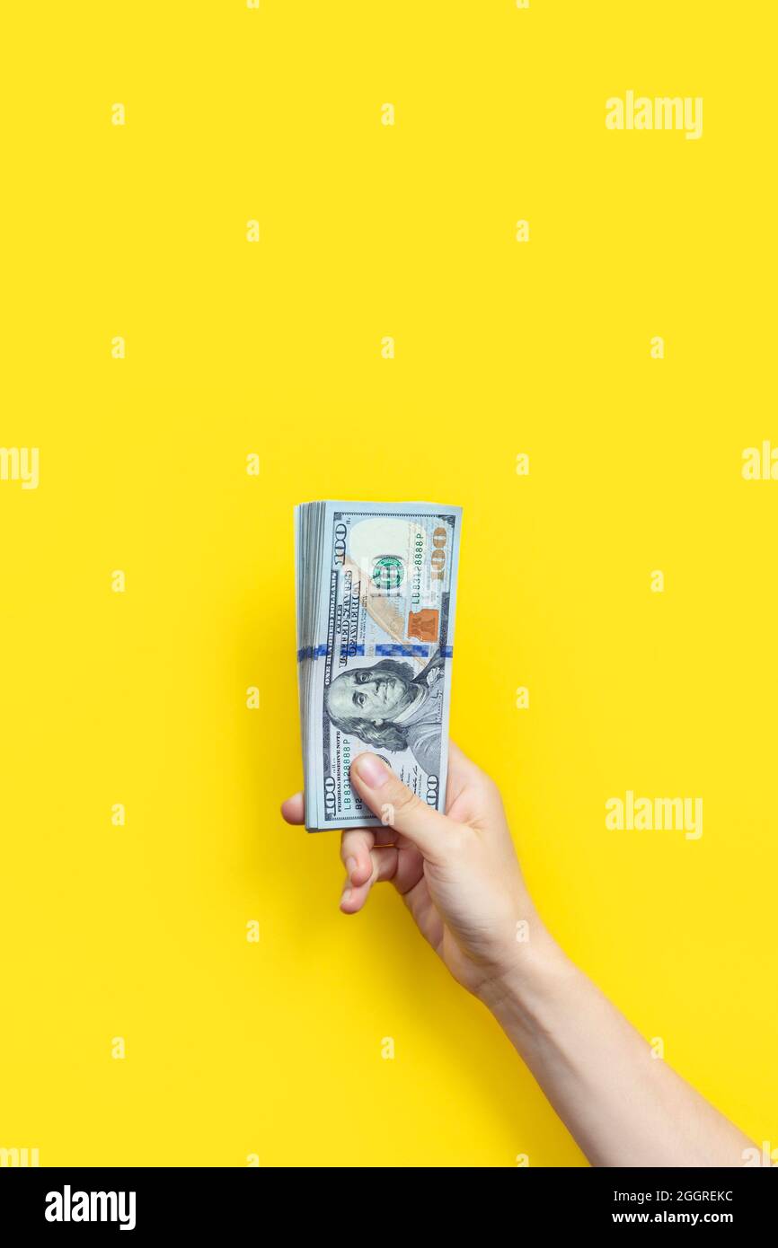 Mano che tiene una grande pila di banconote isolate su sfondo giallo. Ricchezza o concetto di prestito. Banner verticale Foto Stock
