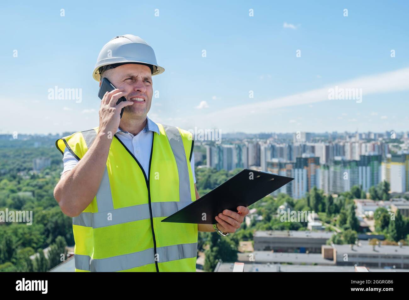 L'uomo in un casco bianco in un cantiere tiene in mano un portadocumenti Foto Stock