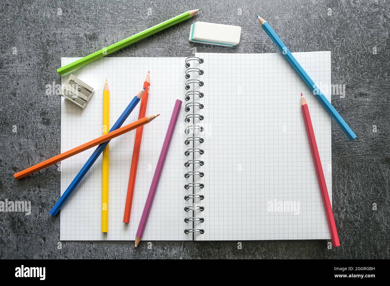 Disposizione piatta di un taccuino vuoto a spirale con spazio di copia, pastelli colorati, affilatore e cancellatore per lavoro creativo, studio o scuola su un tavolo grigio, hi Foto Stock