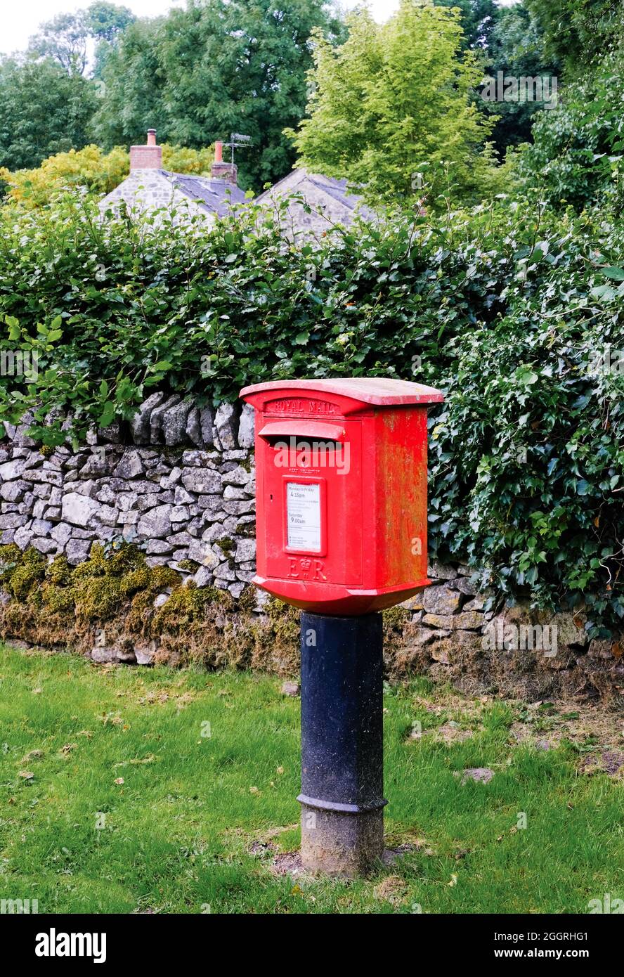 Parwich, Derbyshire, UK Agosto 29 2021 un elegante vecchio box posta rossa su un supporto in ghisa con muro in pietra e cottage coperti di muschio oltre. Foto Stock Parwich, Derbyshire, UK Agosto 29 2021 un elegante vecchio box posta rossa su un supporto in ghisa con muro in pietra e cottage coperti di muschio oltre. Foto Stock