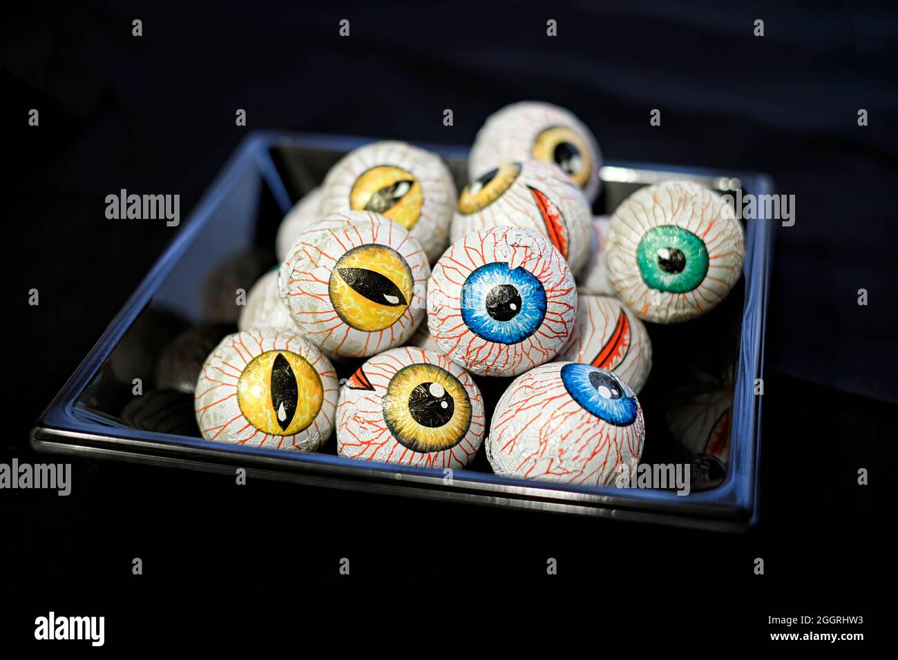 vassoio pieno di spaventosi occhi di cioccolato in diversi colori ad una festa di halloween su sfondo nero, fuoco selettivo, orizzontale Foto Stock