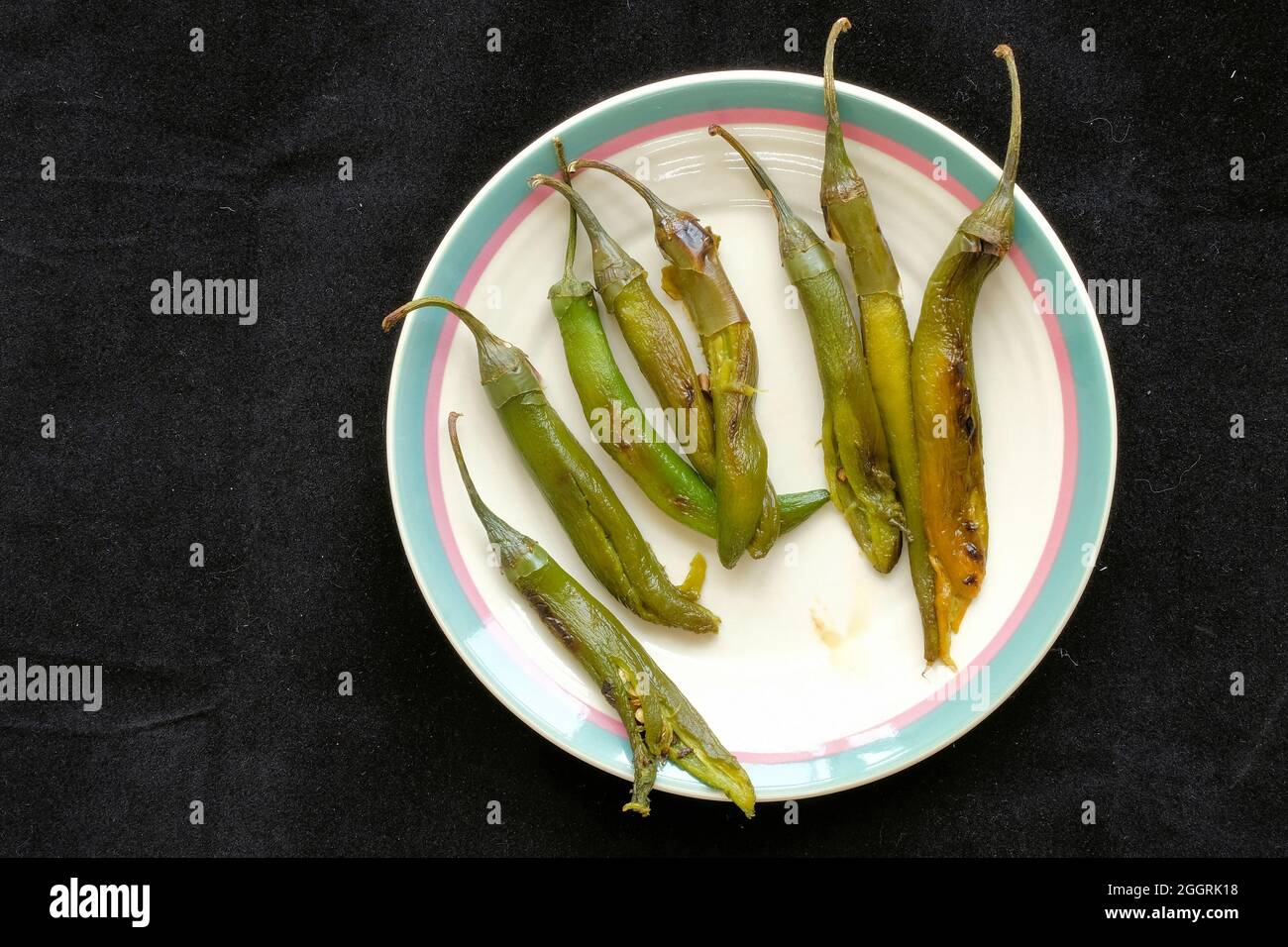 Peperoni serrano arrostiti e sbucciati con gambi su un piatto di ceramica, pronti per la salsa fatta in casa e un ingrediente per il cibo messicano speziato. Foto Stock