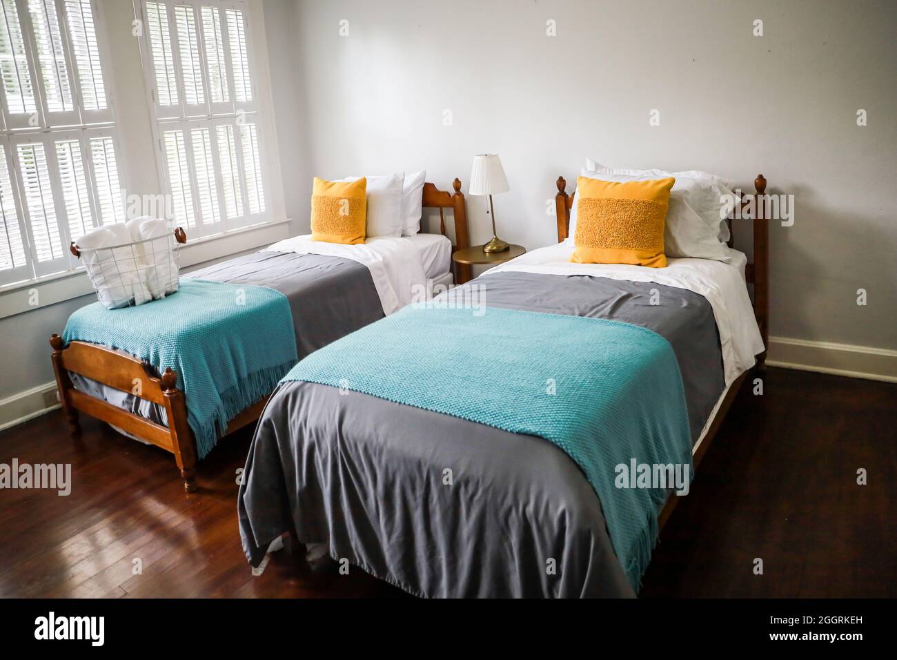 Una camera da letto con due letti singoli con copriletto color turchese e grigio e cuscini decorativi gialli Foto Stock