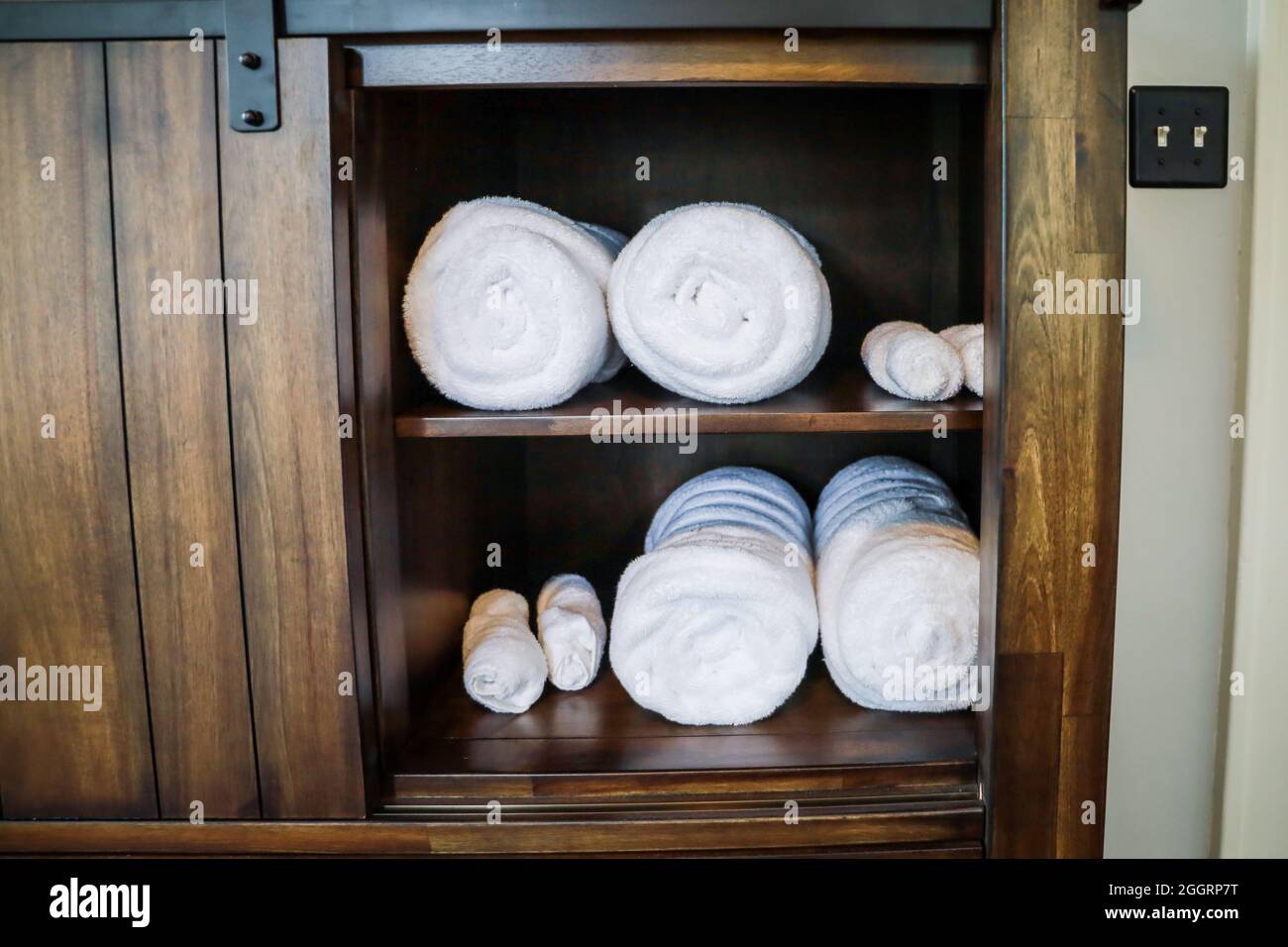 Asciugamani arrotolati bianchi organizzati in un armadietto per gli ospiti Foto Stock