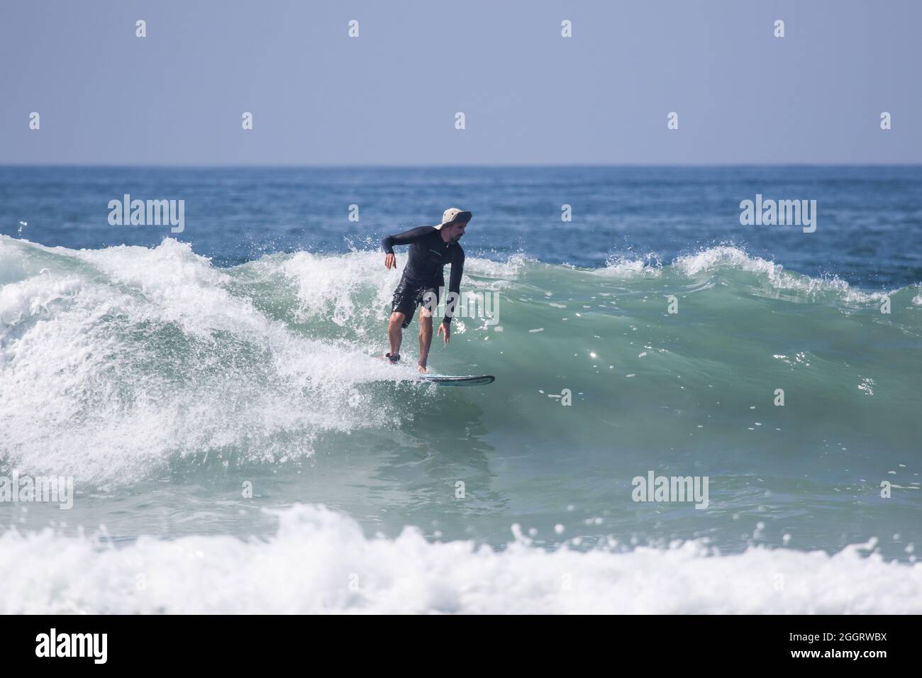 Surfer con cappello di sole che guida un'onda a Huntington Beach, California, Stati Uniti Foto Stock