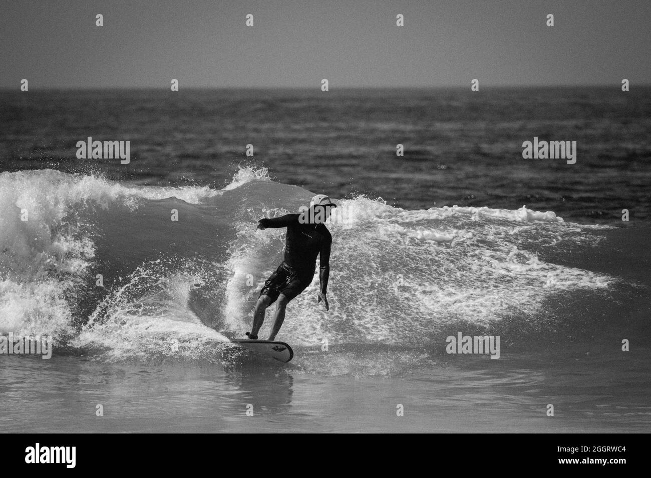 Surfer bianco e nero con cappello da sole che cavalca un'onda a Huntington Beach, California, USA Foto Stock