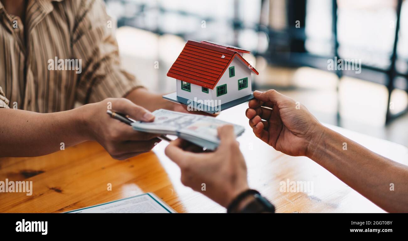 Primo piano delle mani dando modello di casa ad altre mani con soldi. Concetto di immobiliare e affare. Foto Stock