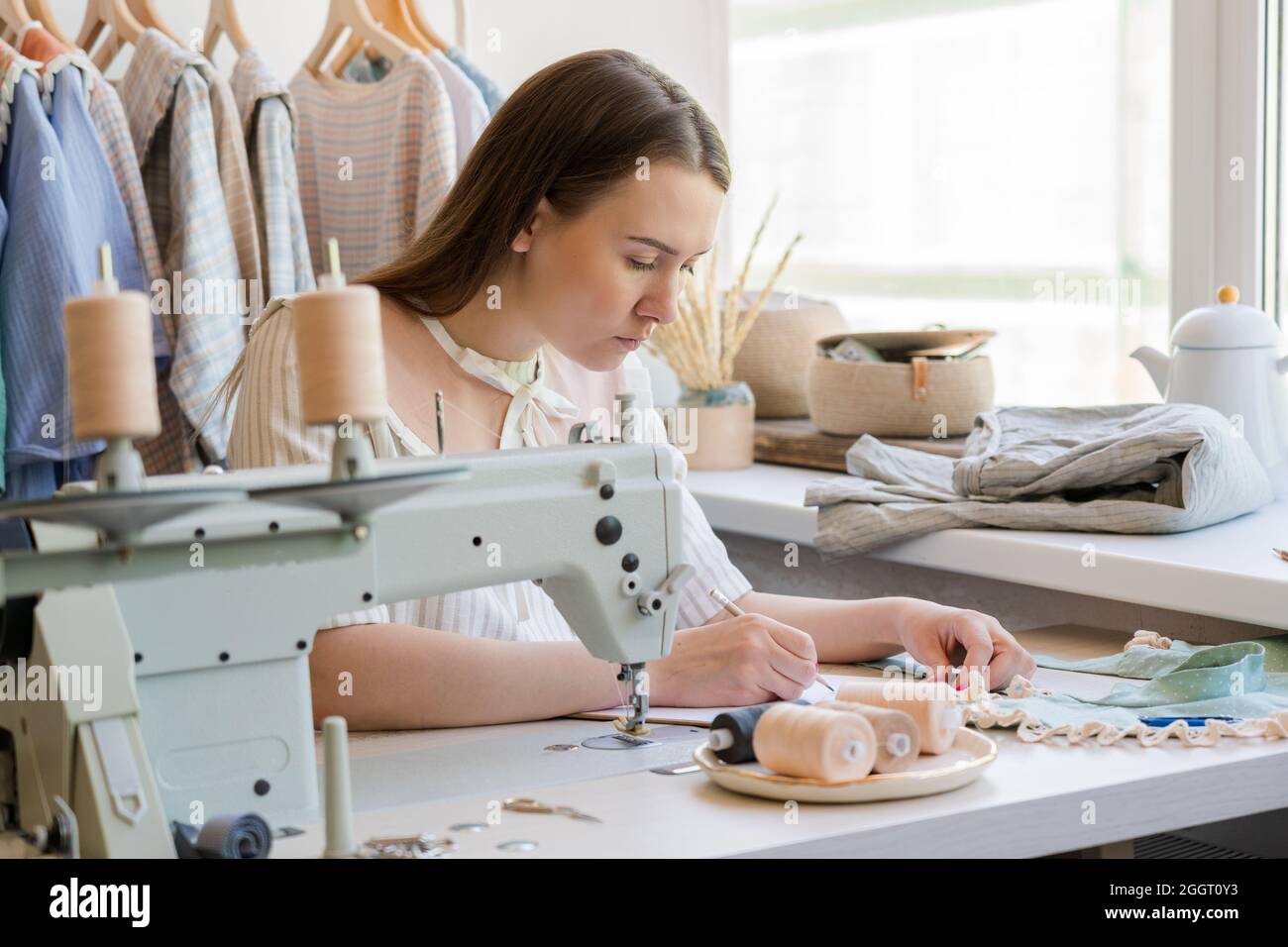 Stilista di moda disegno vestiti schizzo whie seduta al suo posto di lavoro con macchina da cucire Foto Stock