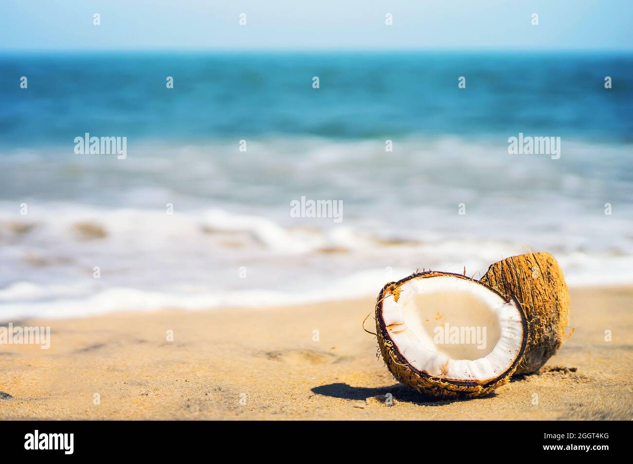 Due metà di un cocco maturo nell'angolo della composizione. Noce si trova su una spiaggia di sabbia bianca su sfondo sfocato di mare blu e cielo blu con c Foto Stock