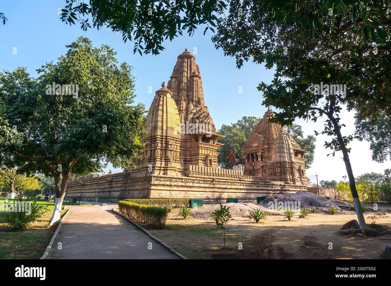Vecchio tempio indù, costruito da Chandela Rajputs, nel sito occidentale in India Khajuraho incorniciata da alberi. Grigio bianco per la struttura beige più giovane e più vecchia Foto Stock