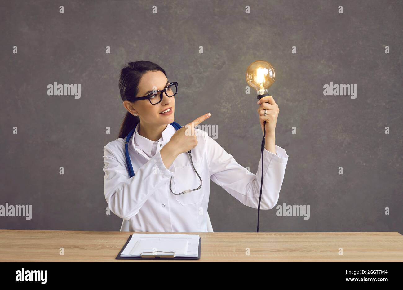 Giovane medico seduto alla scrivania e puntando alla lampadina come concetto di idea innovativa Foto Stock
