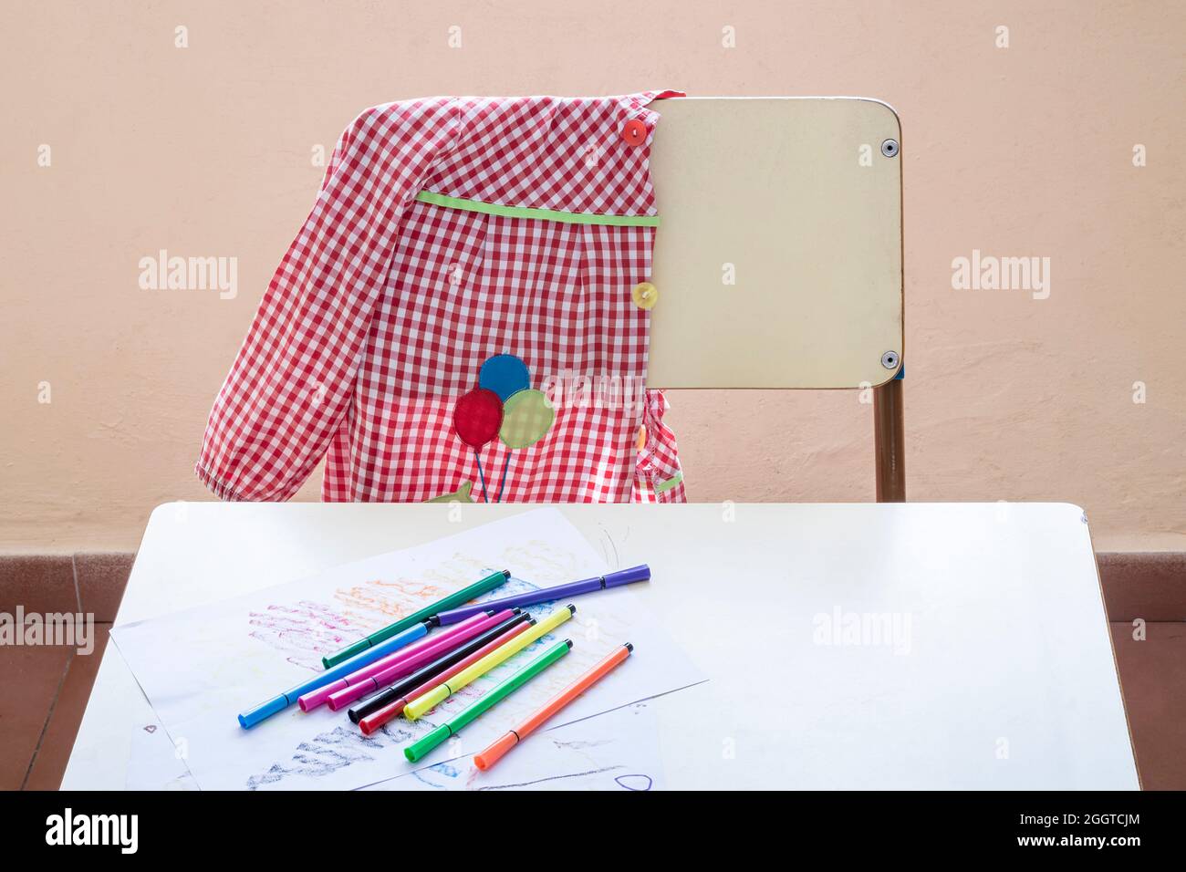 Foto del luogo di studio di uno studente di scuola elementare.nella foto si può vedere una scrivania, un grembiule appeso su una sedia e alcuni marcatori su un disegno Foto Stock