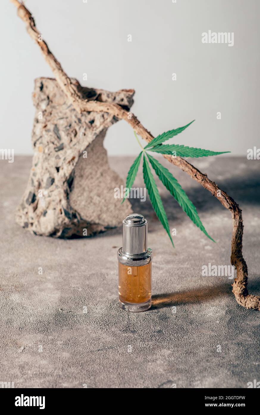 Bottiglia di vetro con olio CBD, tintura THC e foglia di canapa su sfondo di marmo grigio. Minimalismo, naturalezza. Cosmetici a olio CBD. Foto Stock