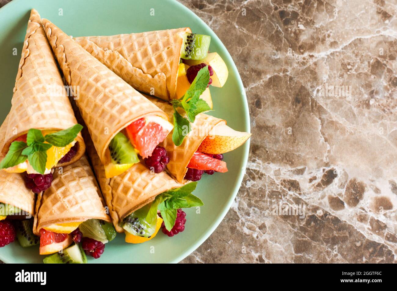 cialda i coni con frutta matura su un piatto su un tavolo di marmo. Foto Stock