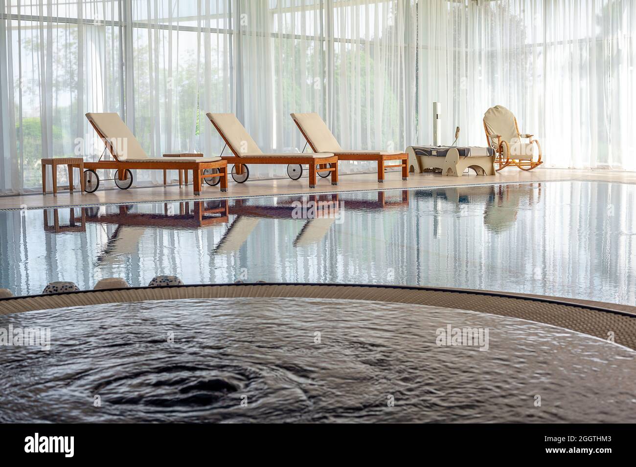 Confortevole piscina interna con jacuzzi, chaise longue, lettino  massaggiante e sedia a dondolo in casa di campagna Foto stock - Alamy