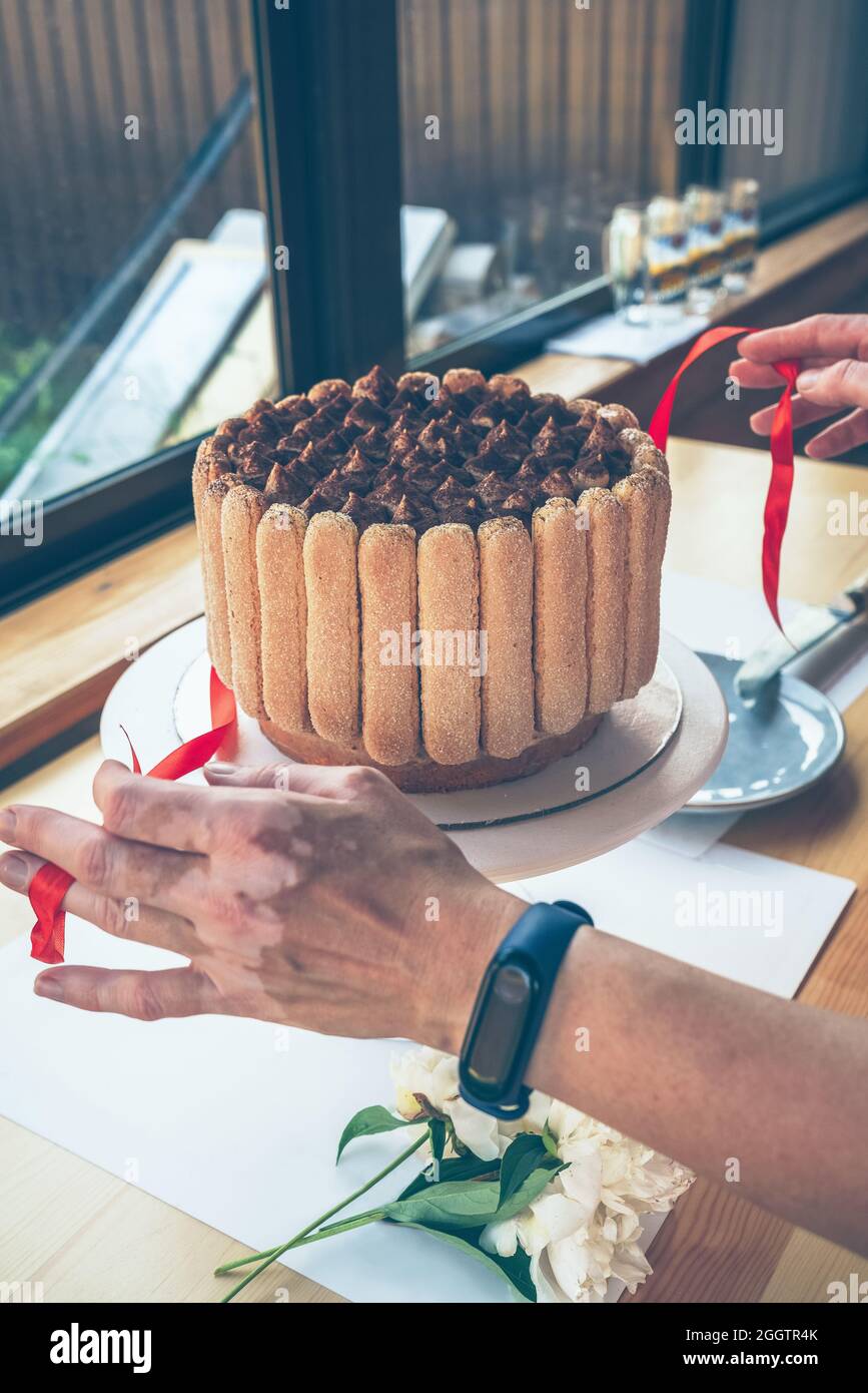 le mani delle donne si slegano decorate con torta tiramisù di prua rossa prima del taglio Foto Stock