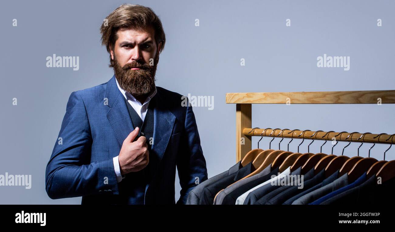 Bell'uomo di moda in costume classico. Abiti maschi appesi in fila. Abbigliamento uomo, boutique. Su misura. Abito elegante da uomo Foto Stock