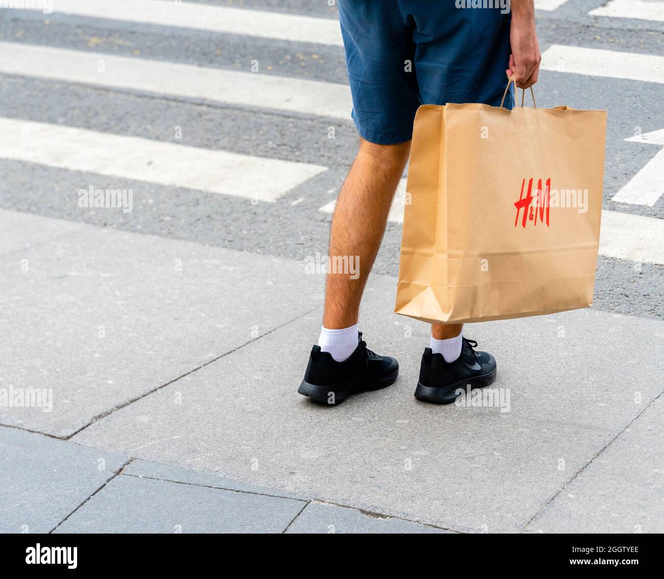 Un uomo in shorts che porta una borsa H & M mentre si trova di fronte al crosswalk, Mosca, Russia. Concetto di consumismo, economia dei consumatori, spesa dei consumatori. Foto Stock