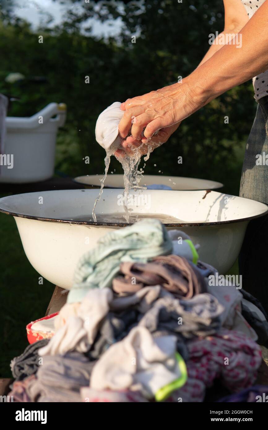 La donna lava i vestiti con le mani in un vecchio lavandino con un sapone all'aperto Foto Stock